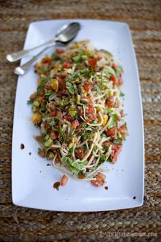 a white plate topped with pasta and vegetables on top of a table next to a fork