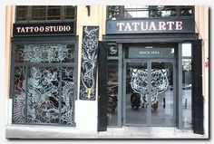 tattoo studio in the middle of an urban area with large windows and intricate designs on the doors