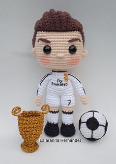 a crocheted doll is next to a soccer ball and a golden trophy on a white background