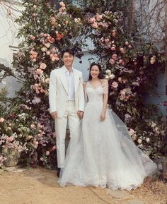 a man and woman standing in front of a floral arch