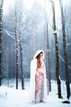 a pregnant woman in a white cloak standing in the snow with her belly exposed and covered up