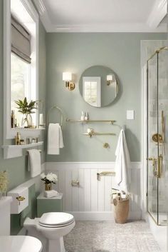 a bathroom with green walls, white fixtures and gold accents on the shower door handles