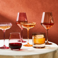 several glasses of different types of wine on a table with a red wall in the background