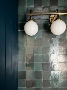 two light fixtures mounted on the side of a wall in a room with tiled walls