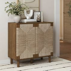 a wooden cabinet sitting on top of a white rug next to a plant and pictures