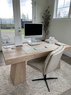 a computer desk with a monitor, keyboard and mouse on it in front of a window