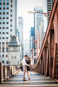 a man and woman are standing on a bridge in the city with tall buildings behind them