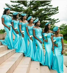 a group of women standing next to each other in blue dresses and hats on steps