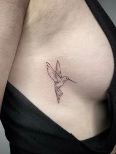 a woman's breast with a small bird tattoo on her left side ribcage