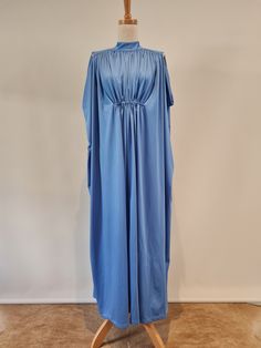 Marisa at Kitty Copeland UK Lovely 1970's Azure Blue jersey cape style maxi dress, from Marisa at Kitty Copeland UK.   This generously flowing 1970's Kaftan or Cape style dress has a slim shoulder line with a drop down armhole, creating a lovely volume through the body and back.  The high neckline has a narrow yoke with fine gathers from this.  The back neck is finished with a keyhole opening with two self covered domed buttons and self fabric loops.  A narrow channel across the centre front wai Vintage Blue Maxi Dress For Formal Occasions, Evening Flowy Maxi Dress With Cape Sleeves, Flowy Maxi Dress With Cape Sleeves For Evening, Flowy Evening Maxi Dress With Cape Sleeves, Blue Evening Maxi Dress, Blue Flowy Maxi Evening Dress, Spring Evening Cape Maxi Dress, Blue Draped Maxi Dress For Evening, Blue Cape Dress For Party