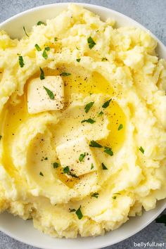 mashed potatoes with butter and parsley in a white bowl on a gray surface