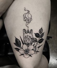 a woman's thigh with a cat and flowers tattoo on her leg, next to a skull