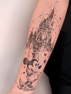 a person with a tattoo on their arm that has a castle and mickey mouse in it