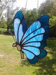 a stained glass butterfly hanging from a chain in a yard with grass and trees behind it