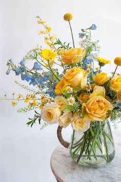 a glass vase filled with yellow and blue flowers on top of a marble countertop