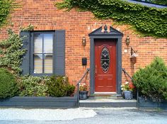 a red door is in front of a brick building with plants and potted trees