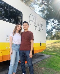 two people standing in front of a yellow and white bus with the words greening tour written on it