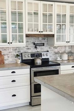 Enter a luxurious white farmhouse kitchen adorned with windowpane cabinetry showcasing intricate grid patterns and complemented by sleek black hardware. The seamless pairing of a neutral gray countertop harmonizes with a whitewashed, exposed brick backsplash.

Commanding attention, a generously sized white kitchen island becomes the focal point, set against the backdrop of light wood flooring. Contemporary decor elements adorn the countertops, and the space is bathed in a gentle, elegant glow. Brick Backsplash White Cabinets, Exposed Brick Backsplash, White Cabinets Wood Countertops, White Brick Backsplash, Light Wood Flooring, White Farmhouse Kitchen, Backsplash Kitchen White Cabinets, Backsplash For White Cabinets, Backsplash With White Cabinets