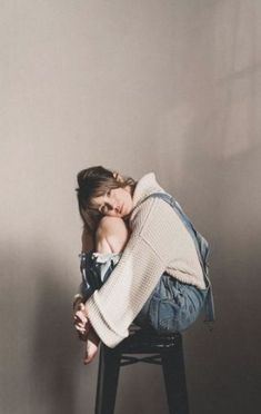 a woman sitting on a stool with her head in her hands while leaning against the wall