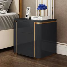 a black and gold side table with blue flowers on it next to a white bed