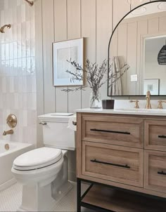 a white toilet sitting next to a bath tub in a bathroom under a mirror on top of a wooden cabinet