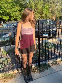 a woman standing next to a fence with her hand on her hip and looking at the ground