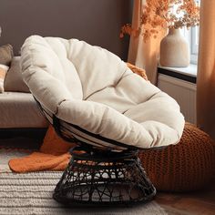 a white chair sitting in front of a window next to a brown rug and pillows