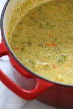 a red pot filled with broccoli soup on top of a white tablecloth