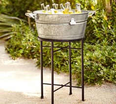 a metal bucket filled with drinks sitting on top of a table next to shrubbery