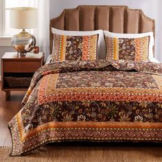 a bed with a brown and orange comforter on top of it next to a night stand