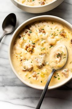 two bowls filled with soup on top of a white table next to silver spoons