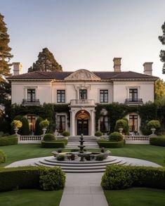 a large white house with lots of trees and bushes in the front yard at sunset