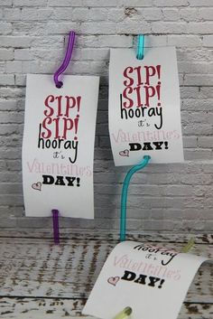 two paper signs hanging from clothes pins on a white brick wall, one says sip sip hooray and the other says valentine's day