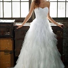 a woman in a white wedding dress standing next to an old trunk with her hands on her hips