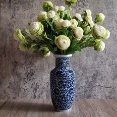 a blue and white vase filled with flowers on top of a wooden table next to a wall