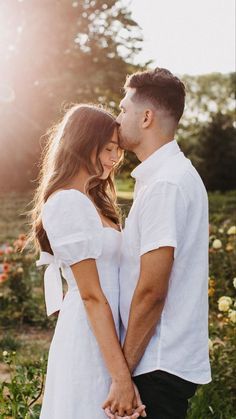 a man and woman holding hands in front of some flowers with the sun shining on them