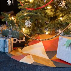 a christmas tree with presents under it on the floor next to a gift bag and wrapping paper