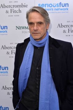 an older man wearing a blue scarf and black jacket standing in front of a white background