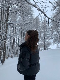 a woman standing in the snow with her back to the camera, looking at trees