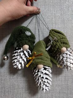 three pine cone ornaments hanging from a string on a wall next to a person's hand