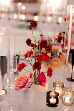 the table is set with candles and vases filled with red, pink and white flowers