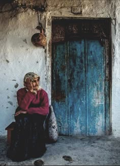 an old woman sitting in front of a blue door