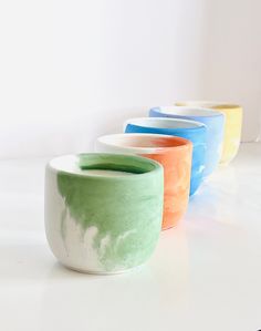 four different colored bowls sitting on top of a white table