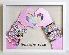 a pink frame with bracelets hanging from it's sides and a hand holding a heart