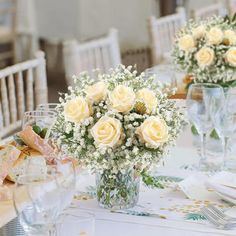 two vases filled with yellow roses on top of a table covered in white napkins