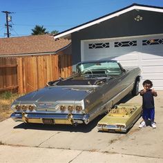 a young boy standing next to an old car in front of a garage with the door open