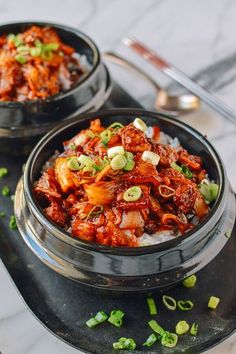 two bowls filled with food sitting on top of a metal tray next to spoons