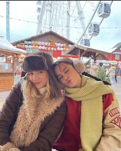 two young women sitting next to each other in front of a ferris wheel