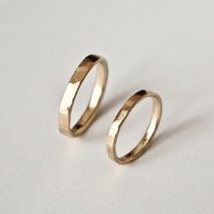 two gold wedding rings sitting on top of a white surface with one ring in the middle