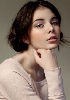 a woman with her hand on her chin looking to the side while wearing a pink sweater